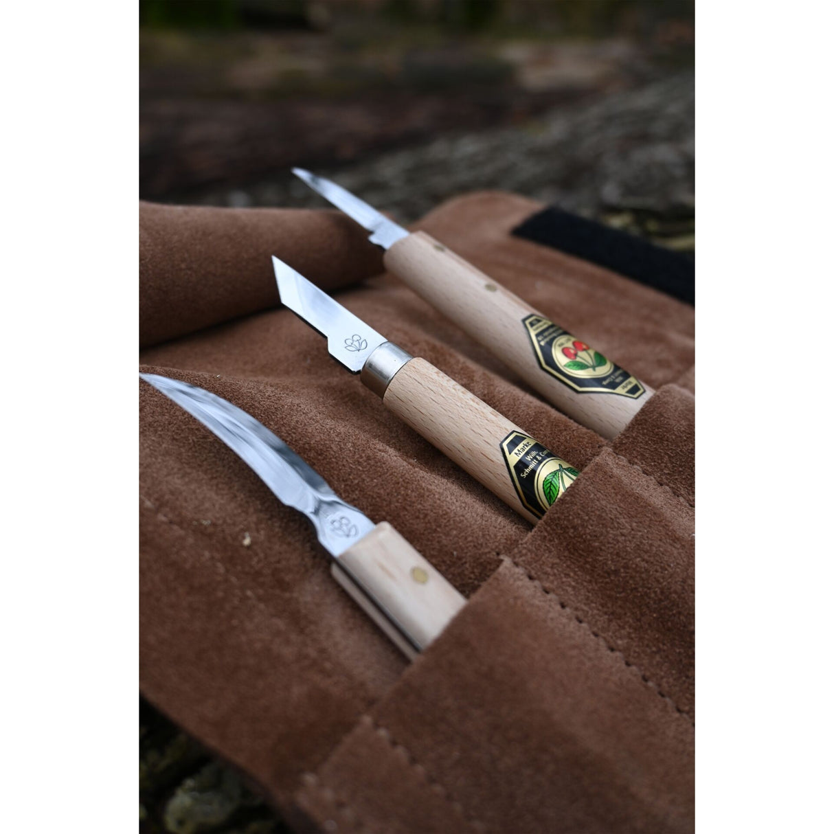 Three carving knives with wooden handles on a brown leather case.