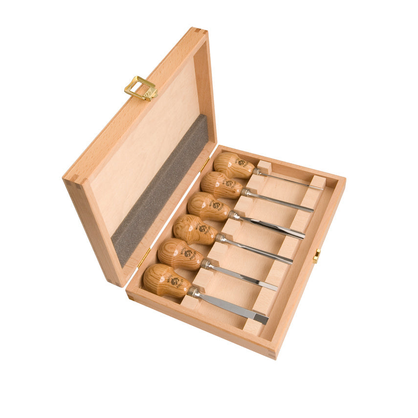 Set of six wooden carving tools and sharpening stone with branded labels in a wooden case.