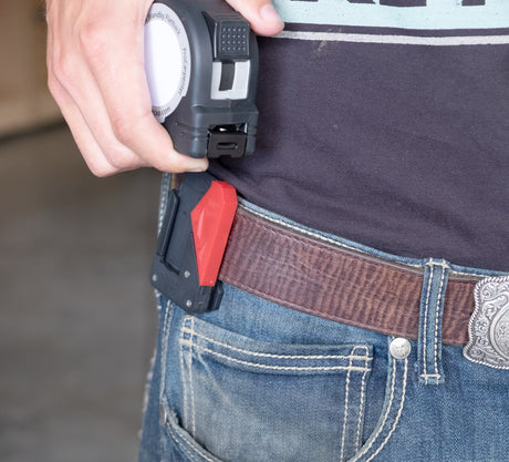 Hand securing tape measure into Fastcap's Tape measure lock on a belt with a blurred background