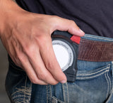 Hand securing tape measure into Fastcap's Tape measure lock on a belt with a blurred background